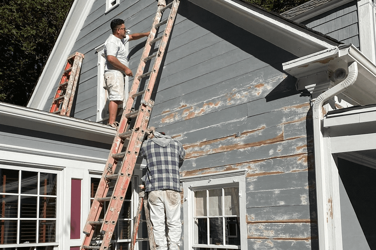 Two workers scraping peeling paint on siding